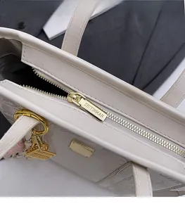 Close-up of golden zipper hardware with brand engraving on white embossed tote bag