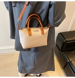 Side view of a beige bucket bag with brown handles worn on shoulder by a model