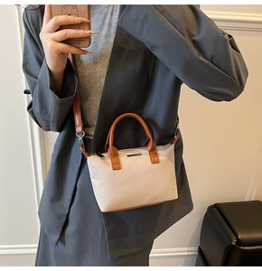Close-up of minimalist beige bucket bag with brown leather handles and metal bar detail