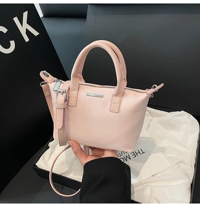 Detail of light pink pebble leather bucket bag with silver metal bar and slim straps