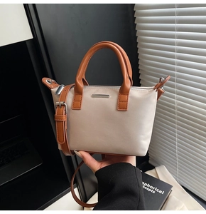 Detail of beige nylon bucket bag featuring brown leather handles and silver metal buckle