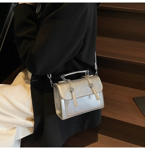 Détail d'un sac à bandoulière argenté métallisé avec rabat à double boucle et poignée