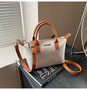 Detail of minimalist bucket bag with cream body, brown straps, and silver hardware