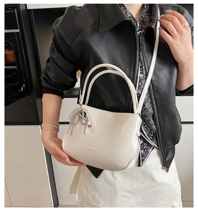 Detail of minimalist cream bucket bag featuring silver key tassel and CLEAVE branding