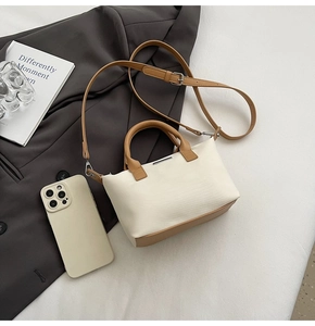 Detail of minimalist cream bucket bag with brown contrast handle on grey blazer context