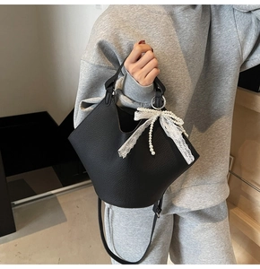Close-up of black lychee texture bucket bag with white lace pearl bow charm detail