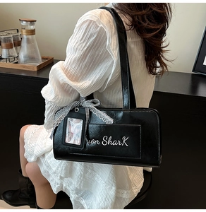 Dettaglio borsa a spalla in pelle nera con ricamo bianco e fiocco in pizzo decorativo