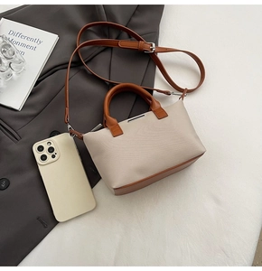 Detail of small bucket bag with beige canvas, brown leather trim and metal accent