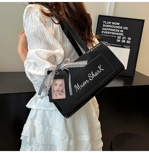 Dettaglio borsa in pelle nera con fiocco in pizzo bianco e ciondolo porta card su vestito