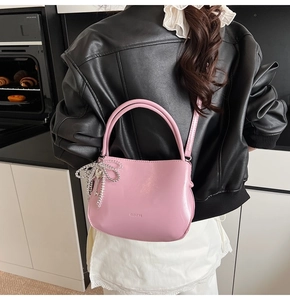 Detail der rosa halbrunden Handtasche mit Silberkette und Logo-Prägung auf glänzendem Leder