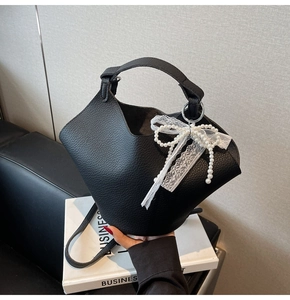 Dettaglio borsa a secchiello in pelle nera con fiocchi di pizzo bianco e perle