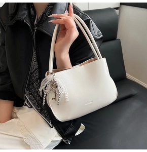 Close-up of minimalist cream bucket bag with silver key charm and brand logo detail