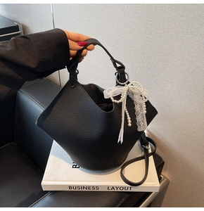 Detail of black lychee grain bucket bag with white lace and pearl bow charm accessory