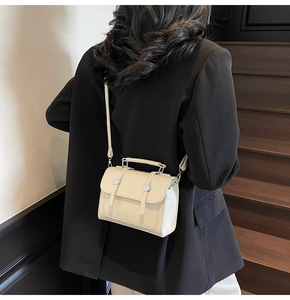 Détail d'un sac bandoulière beige avec boucles en métal argenté et poignée supérieure
