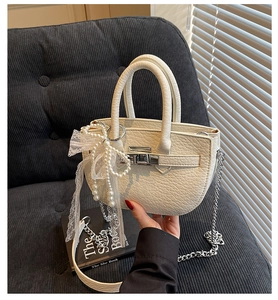 Close-up of beige lychee grain handbag featuring pearl bow charm and silver twist lock