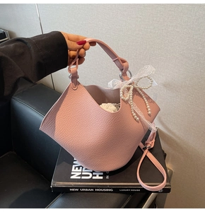 Pink bucket bag with lychee texture featuring pearl lace bow and leather handle
