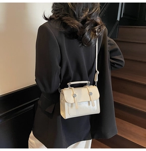 Sac bandoulière chic blanc crème avec poignée et boucle argentée sur un escalier en bois