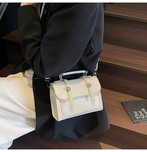 Détail d'un petit sac bandoulière crème avec boucles argentées sur un escalier en bois