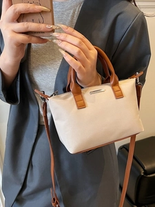Minimalist beige bucket bag with brown leather handles and adjustable shoulder strap