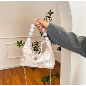 Close-up of floral embroidery on white satin handbag with large white bead handle