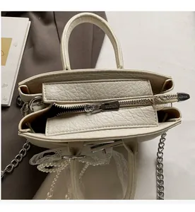 Close-up of beige leather bag featuring metal zipper, pearl chain, and lace charm details