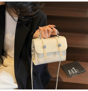 Détail du petit sac carré crème avec boucles argentées posé sur un escalier en bois