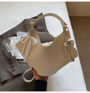 Dettaglio borsa a secchiello beige texture litchi con fiocco di pizzo e perle