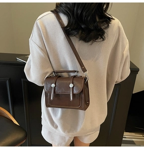 Sac bandoulière vintage en cuir marron avec rabat et boucles argentées porté par le modèle