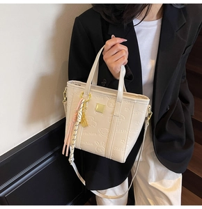 Detail of cream embossed bucket bag with bear patterns and pink tassel pendant
