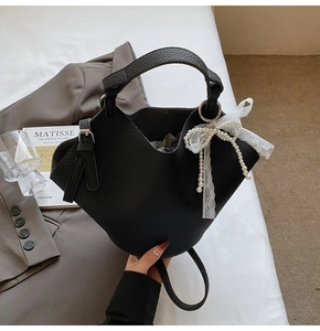 Dettaglio borsa a secchiello in pelle nera con perle e decorazione fiocco in pizzo