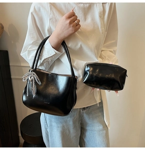 Close-up of black glossy leather bucket bag with silver bow charm and inner pouch