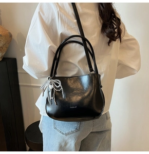 Detail of minimalist black bucket bag with beaded bow pendant and CLEAR AK logo detail