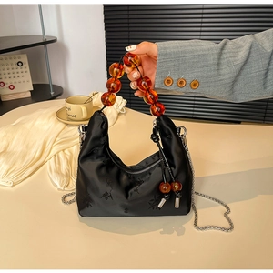 Detailed view of black silk embroidery dumpling bag with amber beaded handle and metal chain