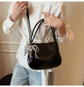 Detail of glossy black PU bucket bag featuring a silver beaded bow charm with key pendant