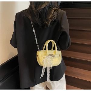 Close-up of yellow leather bucket bag with elegant pearl bow and silver chain detail