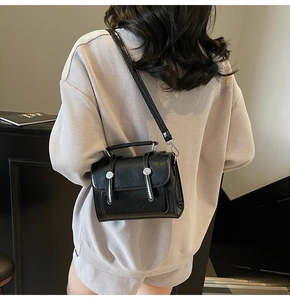 Modèle portant un petit sac bandoulière en cuir noir brillant texturé vu de l'arrière