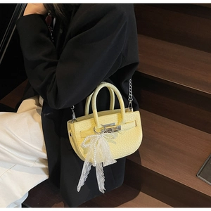 Macro view of light yellow textured leather handbag with silver lock and pearl lace bow