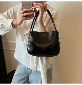 Detail einer schwarzen halbrunden Handtasche mit silbernem Perlenanhänger und glattem Leder
