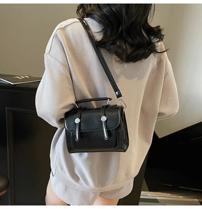 Détail d'un sac à bandoulière noir brillant avec boucles argentées porté par un mannequin