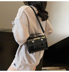 Détail d'un sac à main noir brillant en cuir avec boucles argentées porté par un mannequin