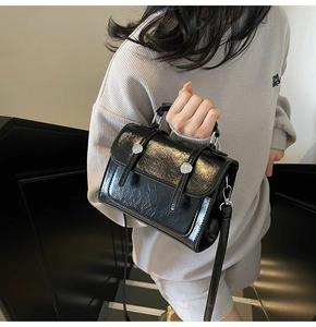Détail du sac à bandoulière minimaliste en cuir verni noir avec boucles argentées