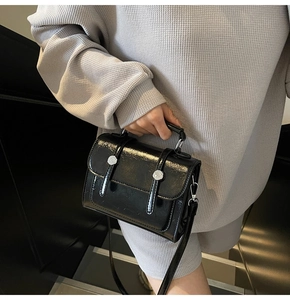 Détail d'un sac à main en cuir verni noir avec boucle fleur argentée et poignée