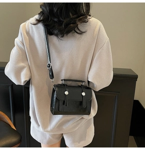 Gros plan d'un sac à bandoulière minimaliste en cuir verni noir avec boucle argentée