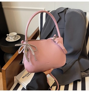 Detail der rosa Leder-Beuteltasche mit Perlen-Schleifenanhänger und Clearux-Logo auf Stuhl