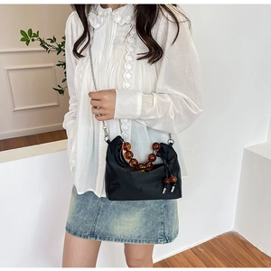 Detail of black embroidered crossbody bag featuring amber bead handle and silver chain