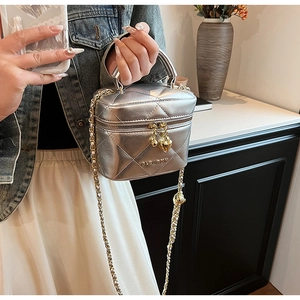 Détail d'un sac argenté matelassé avec breloque cœur et bandoulière en chaîne dorée