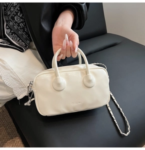 Close-up of white Boston bag with round handles and metal chain strap on black leather