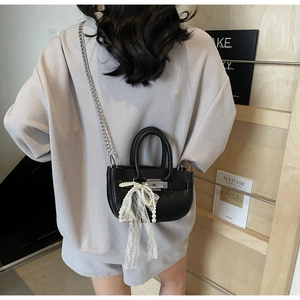 Detail of black mini bucket bag with lace bow and pearl charm on a model