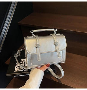 Détail d'un sac à main argenté métallisé avec boucles rondes sur fond de bois et livre