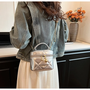 Détail d'un sac argenté matelassé avec pendentifs en cœur et bandoulière dorée